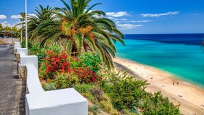 A coastal road with white barriers, palm trees, and a beach with clear turquoise water. - SBH Club Paraíso Playa - All Inclusive (Pajara)