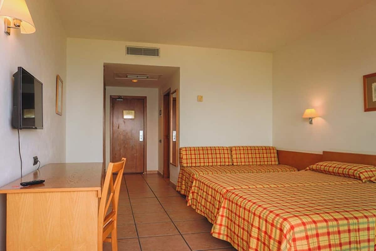 A hotel room with a bed, a desk, a chair, a television, and a door.
