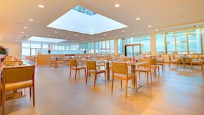 A spacious indoor area with multiple tables and chairs, large windows, and a skylight. - SBH Monica Beach Hotel (Pajara)