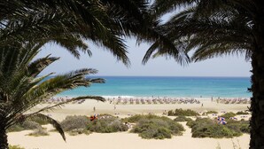 A beach with umbrellas and people, palm trees, and a clear sky. - SBH Monica Beach Hotel (Pajara)