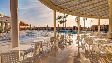 Un espace extérieur abrité, doté de tables et de chaises, d’une piscine et de palmiers.