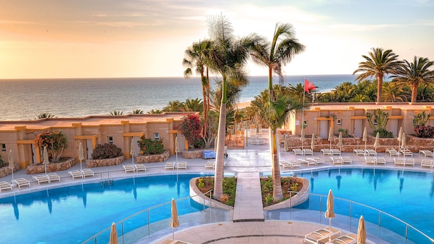 A resort pool with sun loungers and palm trees, overlooking the ocean. - SBH Monica Beach Hotel (Pajara)