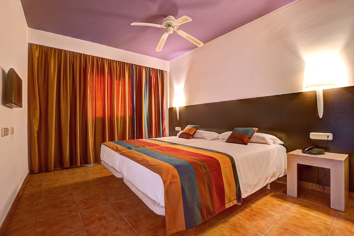 A hotel room with a bed, a nightstand, a ceiling fan, and a wall-mounted light.