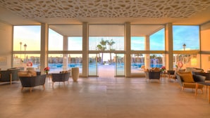 A spacious lobby with large windows, comfortable seating, and a view of the pool area. - SBH Monica Beach Hotel (Pajara)