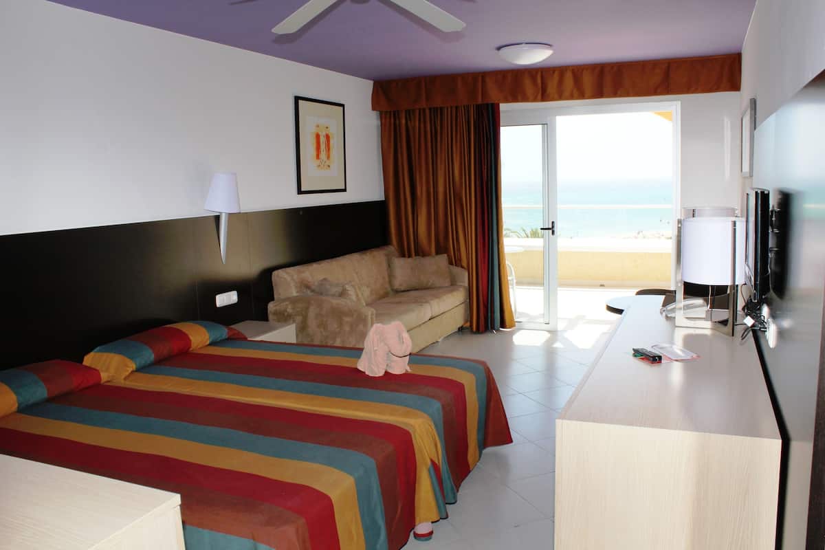 A hotel room with a bed, a sofa, a desk, and a view of the beach.