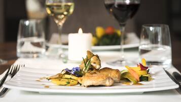 A white plate with a chicken dish, vegetables, and a candle on a table.