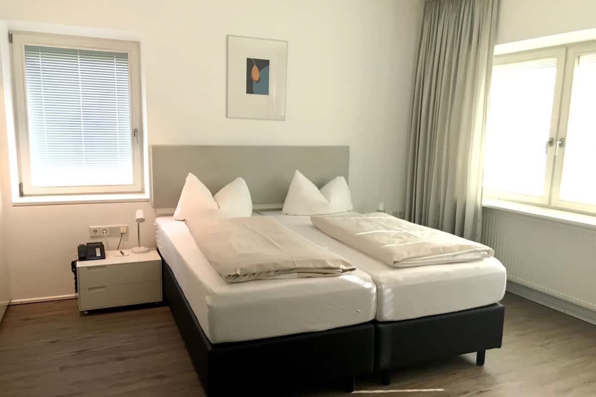 A double bed with a grey headboard, a bedside table with a lamp, and a window with curtains.