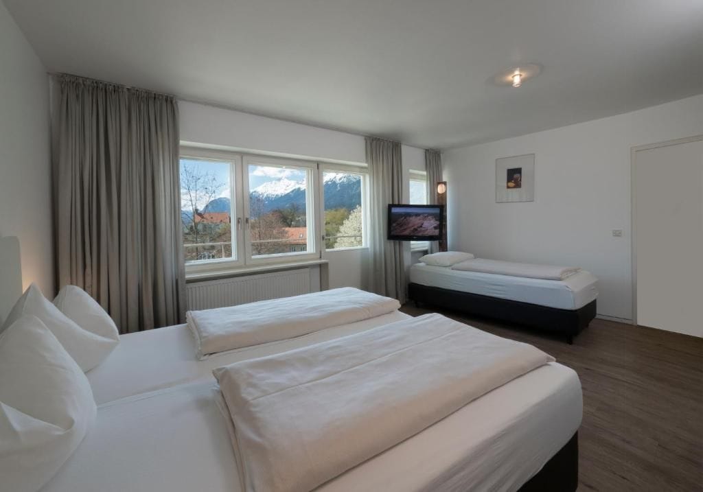 A hotel room with two beds, a television, and a view of mountains.