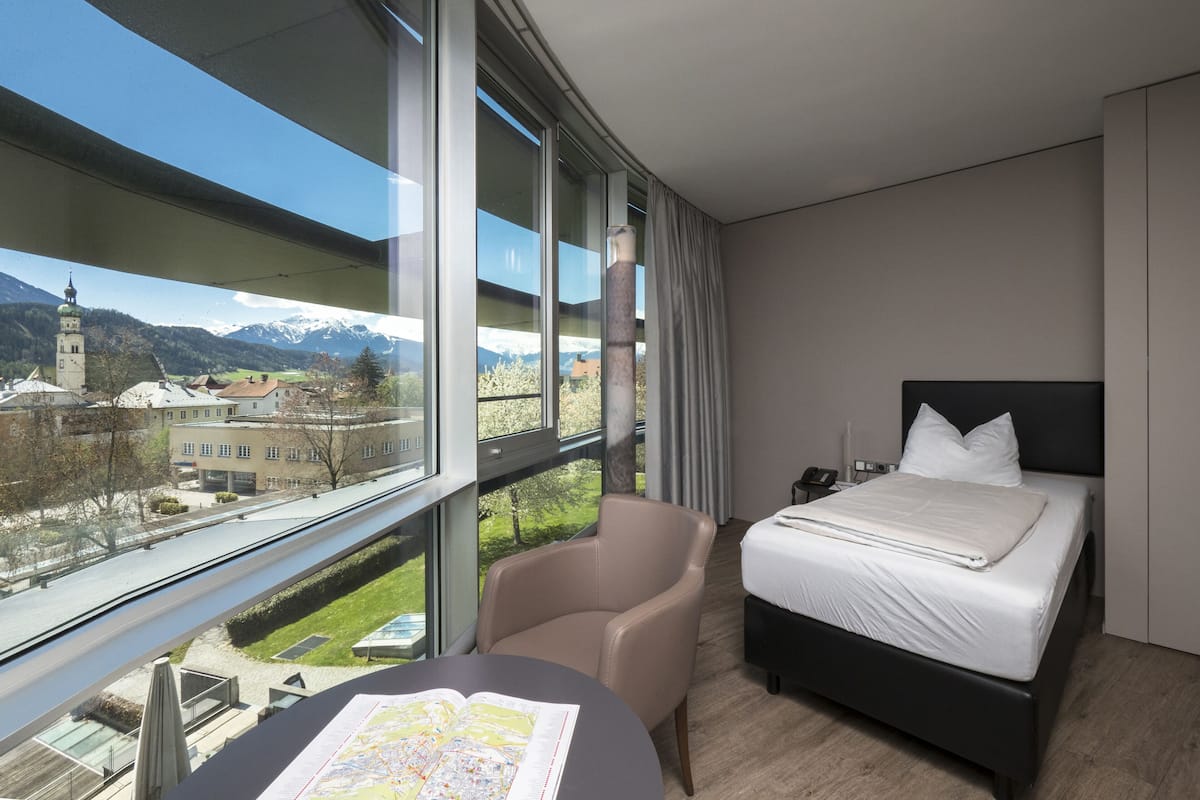 A hotel room with a large window, a bed, a chair, and a table with a map.