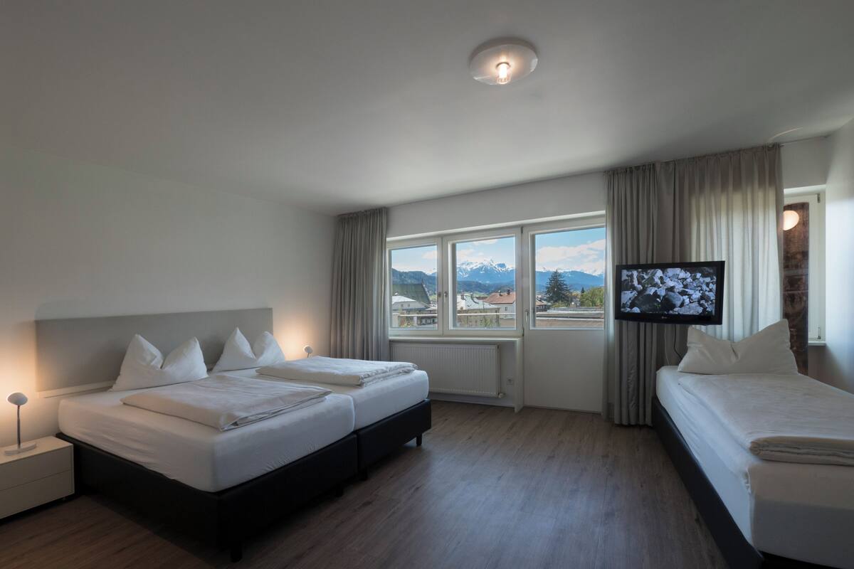 A hotel room with a large bed, a smaller bed, a TV, and a window with a view of mountains.