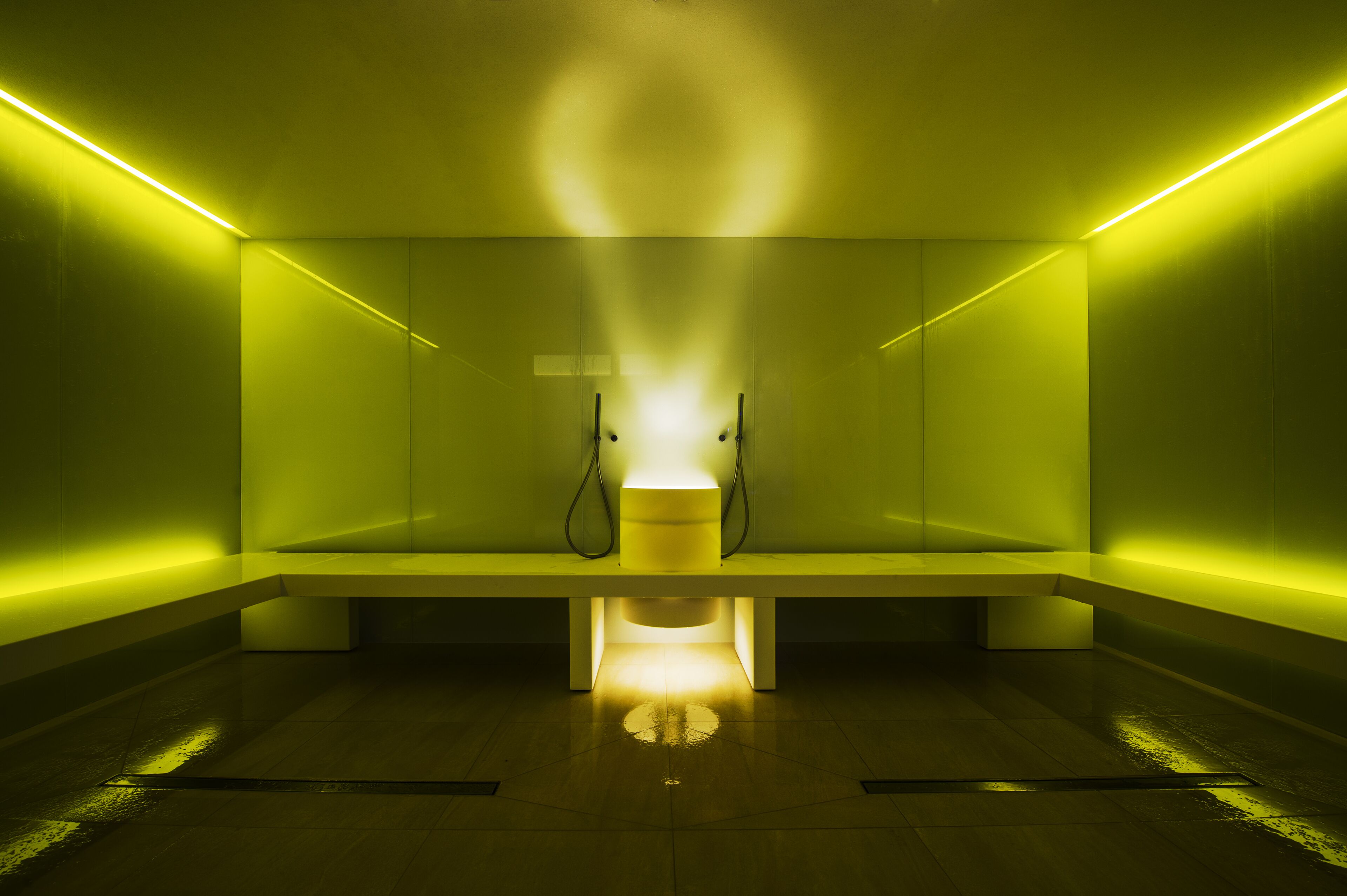 A modern, minimalist room with a bench, a central light fixture, and a reflective floor.