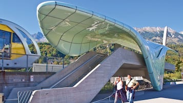 A modern architectural structure with a curved roof, a staircase, and a view of mountains in the background.