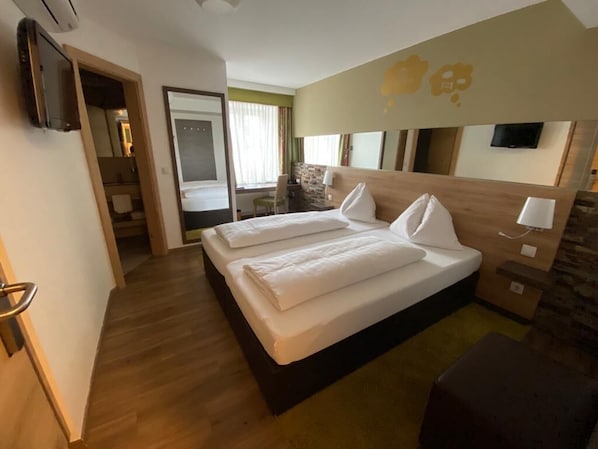 Habitación de hotel con una cama doble, un televisor montado en la pared y un cabecero de madera.