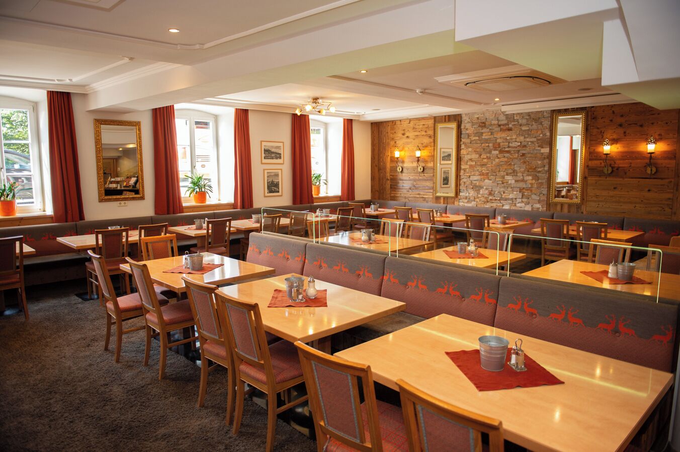 A restaurant with wooden tables and booths, stone walls, and large windows with red curtains.