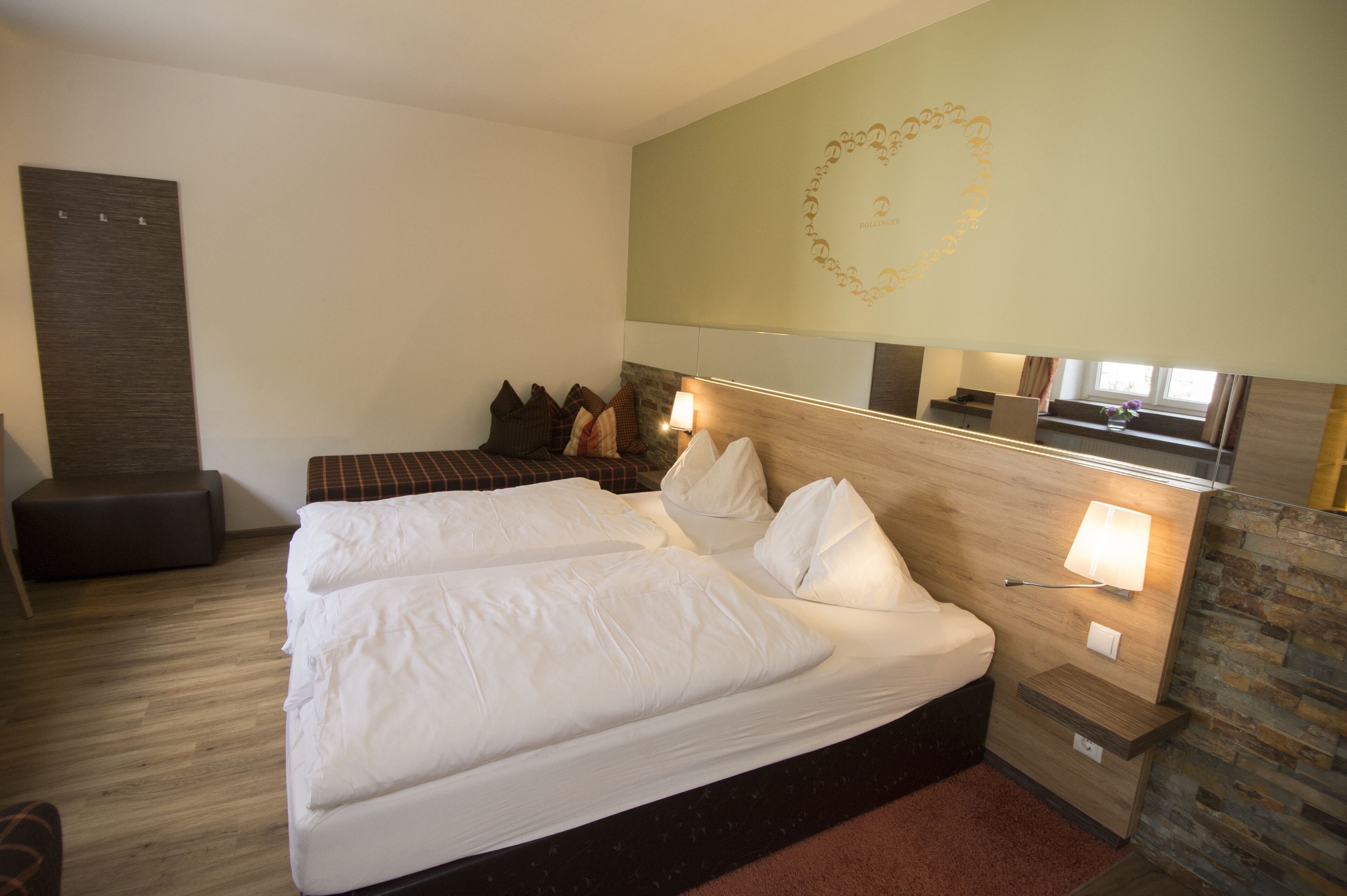 Habitación de hotel con una cama grande, un pequeño rincón de descanso, un espejo y una pared con diseño decorativo.