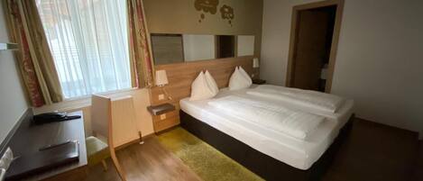 Habitación de hotel con cama, escritorio, silla, radiador y ventana con cortinas.