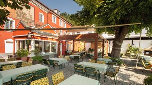 Un patio exterior con mesas y sillas, una pérgola y un edificio con un mural de fondo.