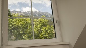 Una ventana con vistas a una cadena montañosa y árboles verdes y frondosos.