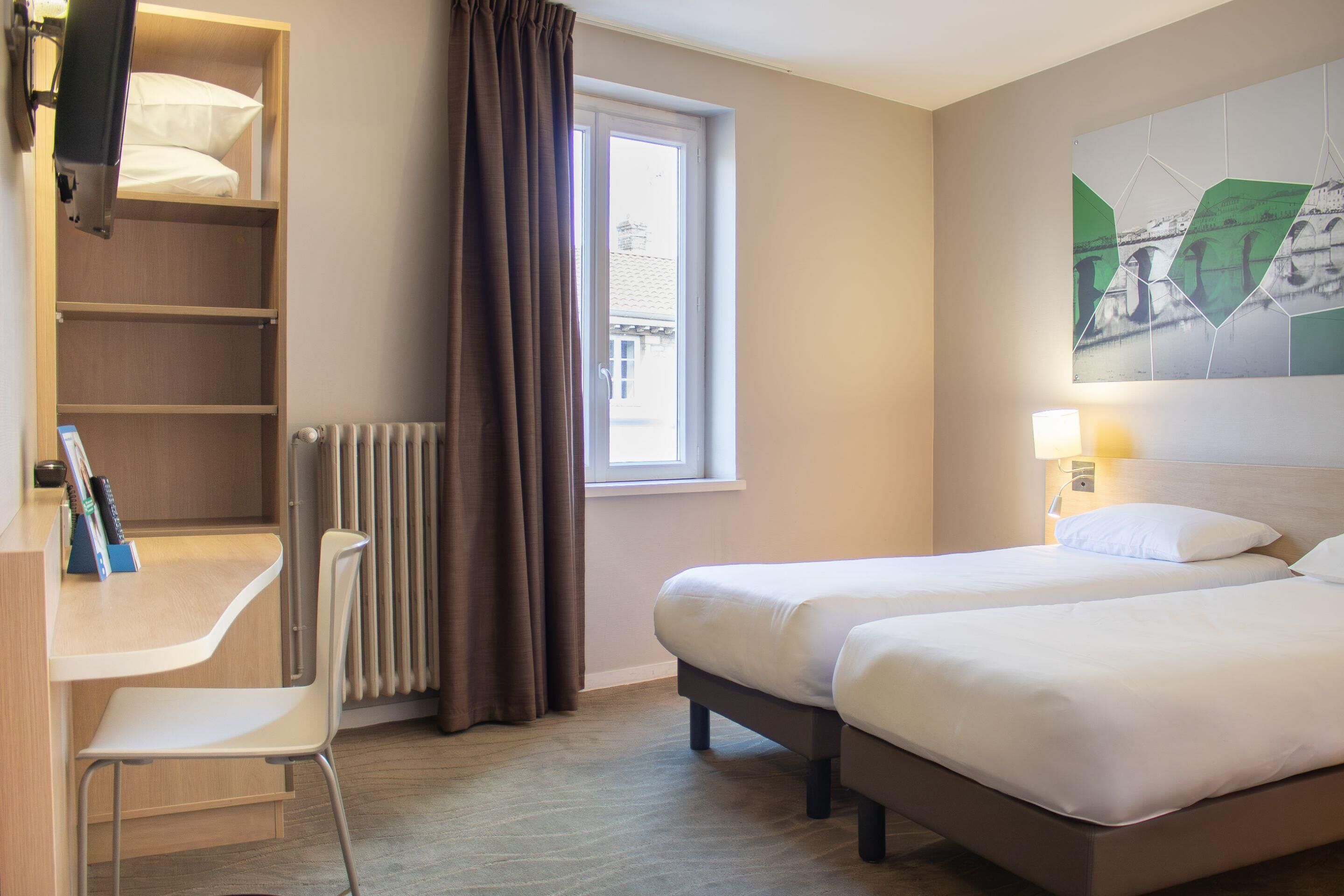 Ein Hotelzimmer mit zwei Betten, einem Schreibtisch, einem Stuhl, einem Heizkörper, einem fenster mit Vorhängen und einem Wandbild.