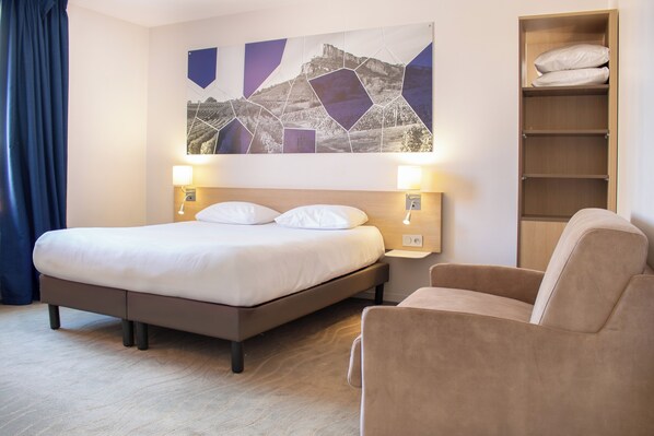 Une chambre d’hôtel comprenant un lit, des lampes de chevet, une chaise et une œuvre d’art murale.