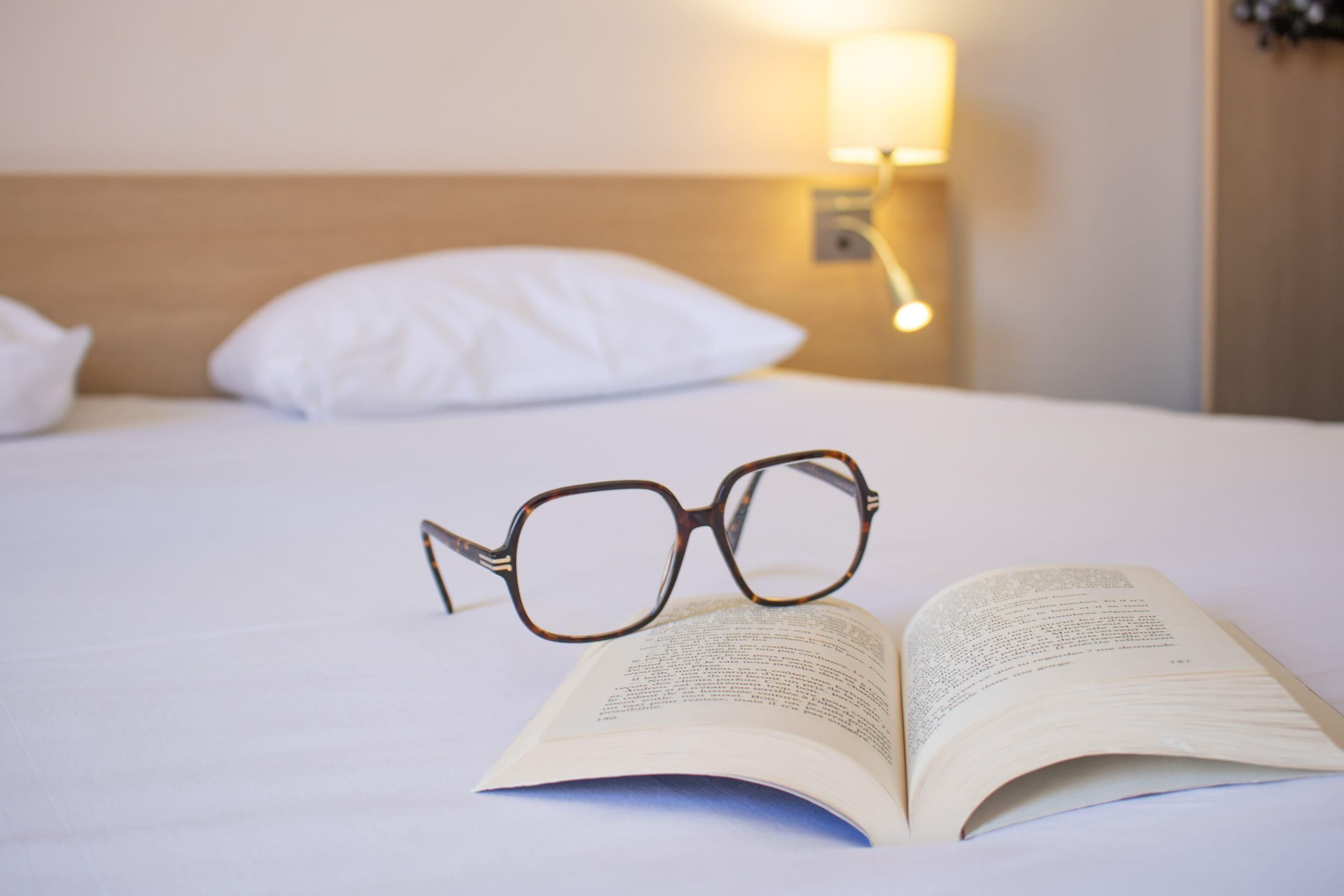 A bed with white bedding, a pair of glasses, and an open book.