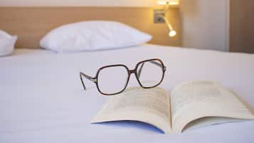 A bed with white bedding, a pair of glasses, and an open book.