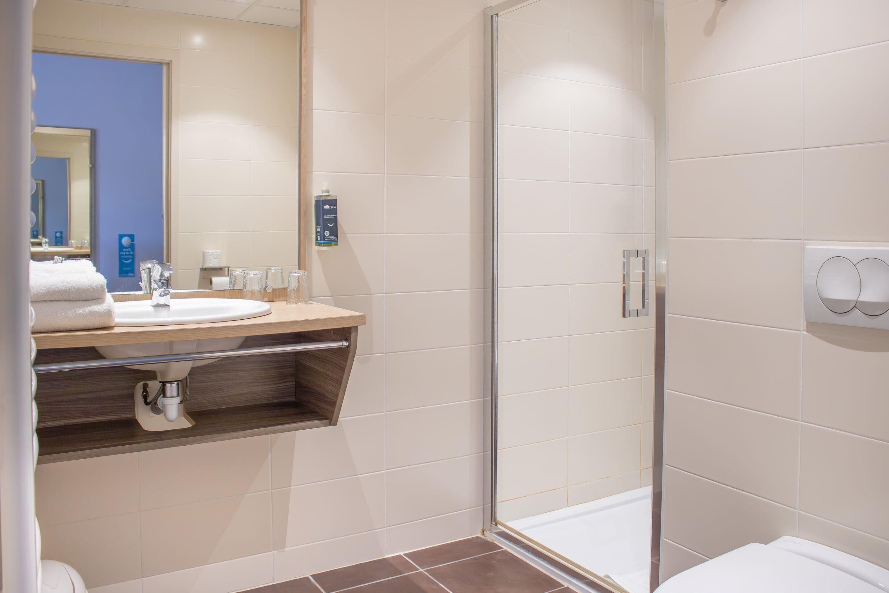 Een moderne badkamer met een douchecabine van glas, een wastafel met spiegel en een handdoekrek.