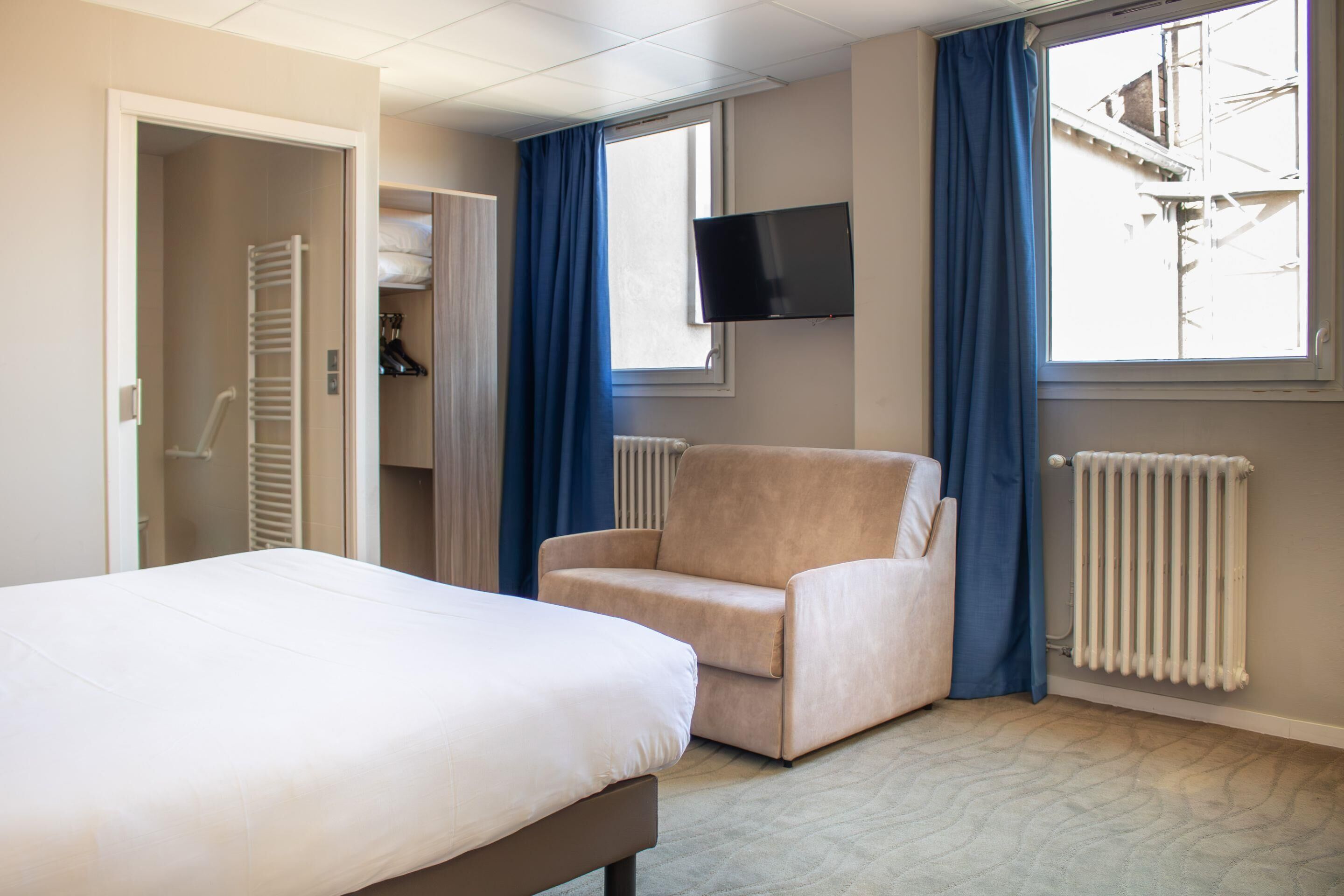 A hotel room with a bed, a chair, a TV, and a window with curtains.