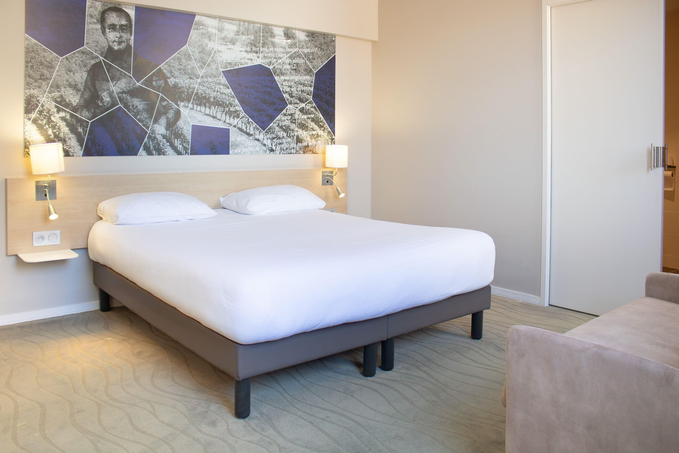 A neatly made bed with white linens, two bedside lamps, and a wall-mounted abstract art piece.