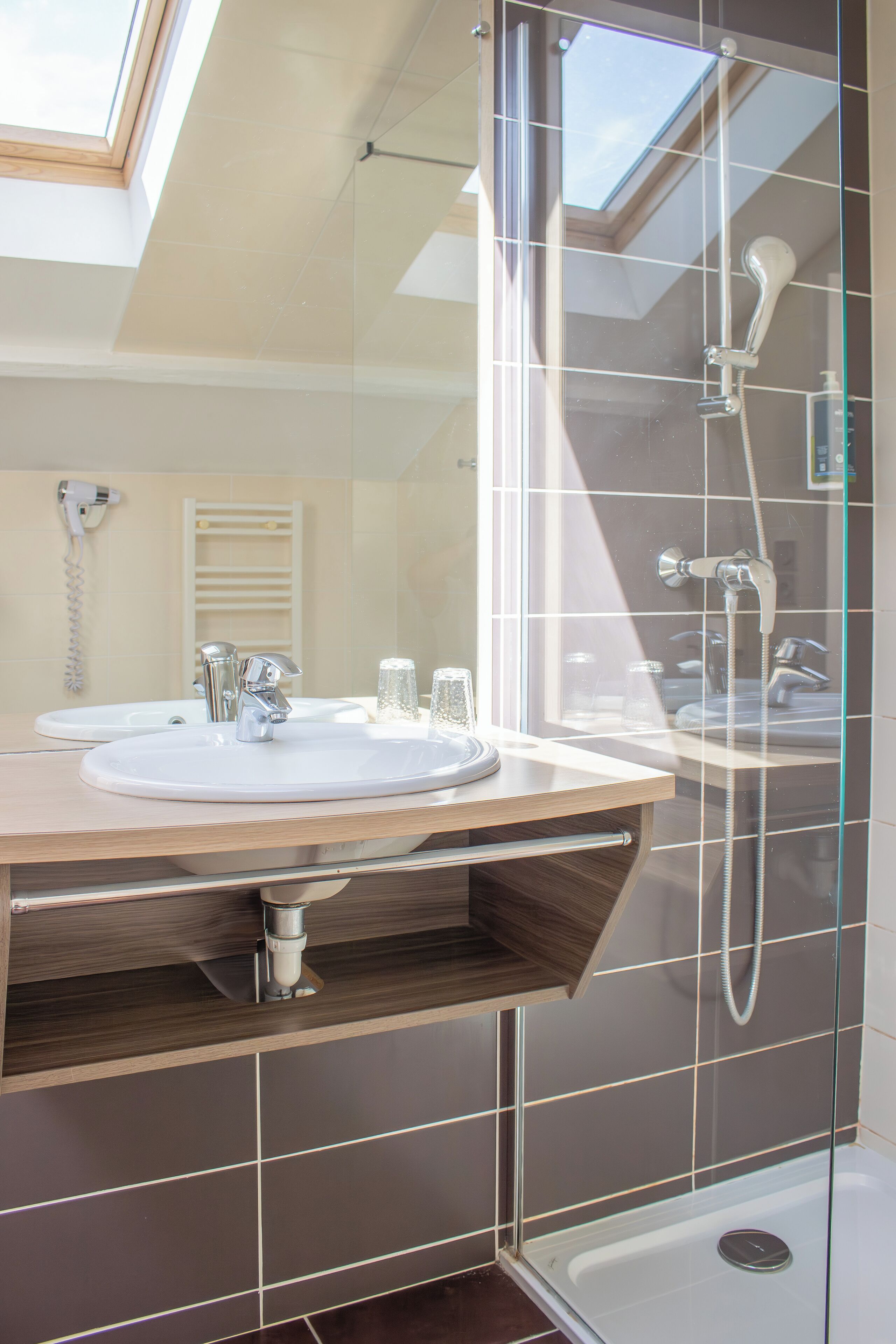 Une salle de bain moderne dotée d’une lucarne, d’une douche en verre et d’un meuble-lavabo avec un évier et un miroir.