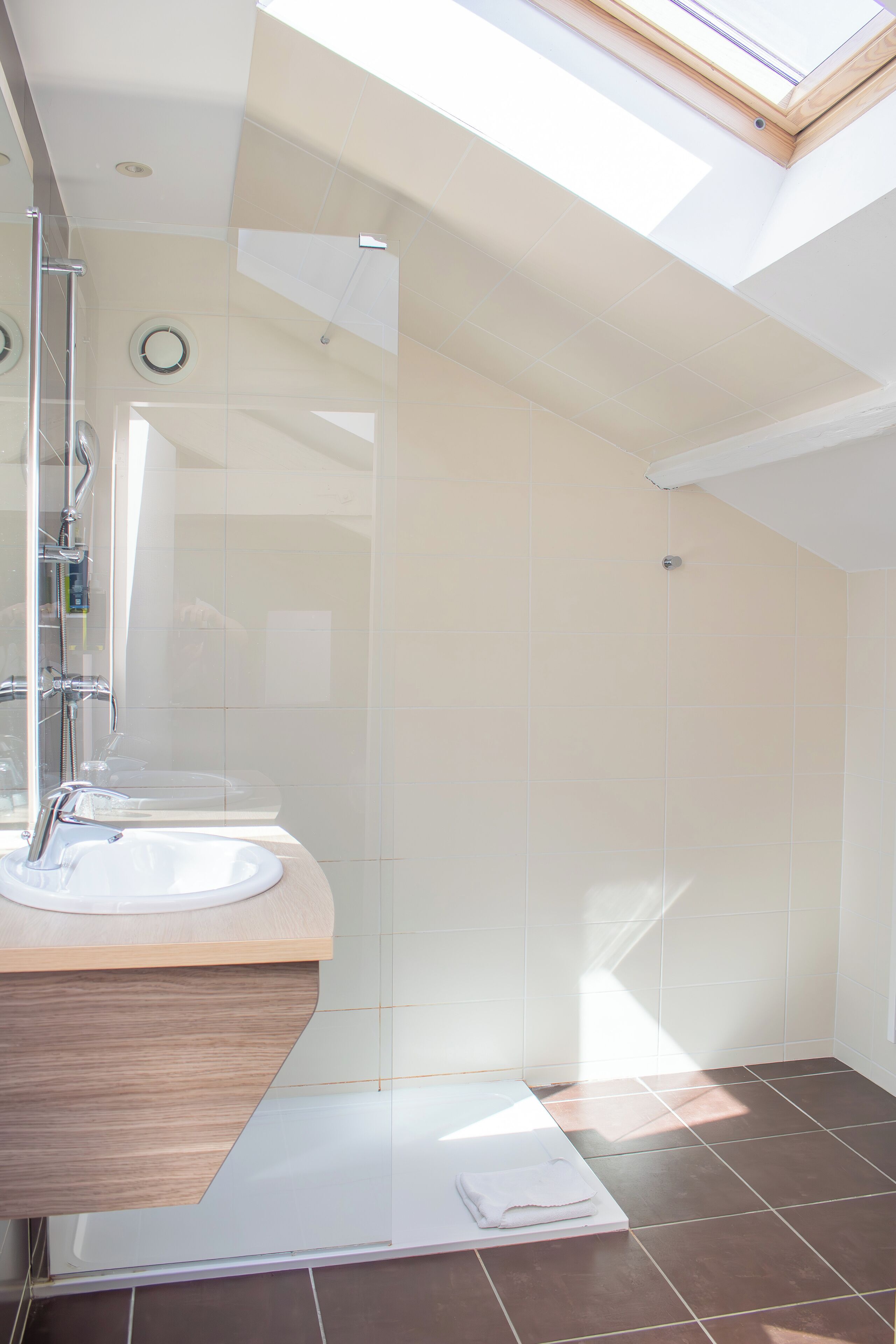 Un baño moderno con tragaluz, cabina de ducha de cristal y tocador de madera con lavamanos.