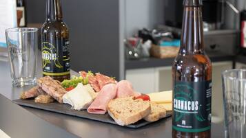 Een charcuterieplank met diverse vleessoorten, kazen en brood, vergezeld van twee flessen Carminius bier en twee glazen op een keukentafel.