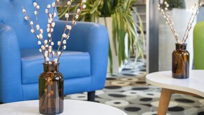Una zona de recepción con un sofá azul, una mesa blanca y dos jarrones con ramas.