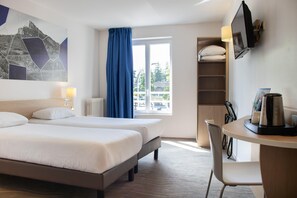 Une chambre d’hôtel avec deux lits, un bureau avec une chaise, une télévision et une fenêtre donnant sur l’extérieur.