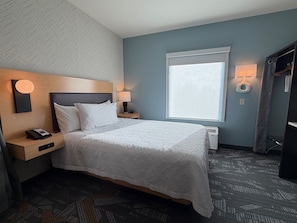 Een hotelkamer met een bed, nachtlampjes, een telefoon, een klein tafeltje en een raam met jaloezieën.