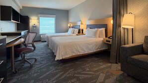 Een hotelkamer met twee bedden, een bureau, een stoel, een lamp en een raam met gordijnen.