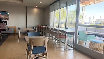 A spacious indoor seating area with tables and chairs, large windows offering a view of the outside, and a ceiling with recessed lighting.