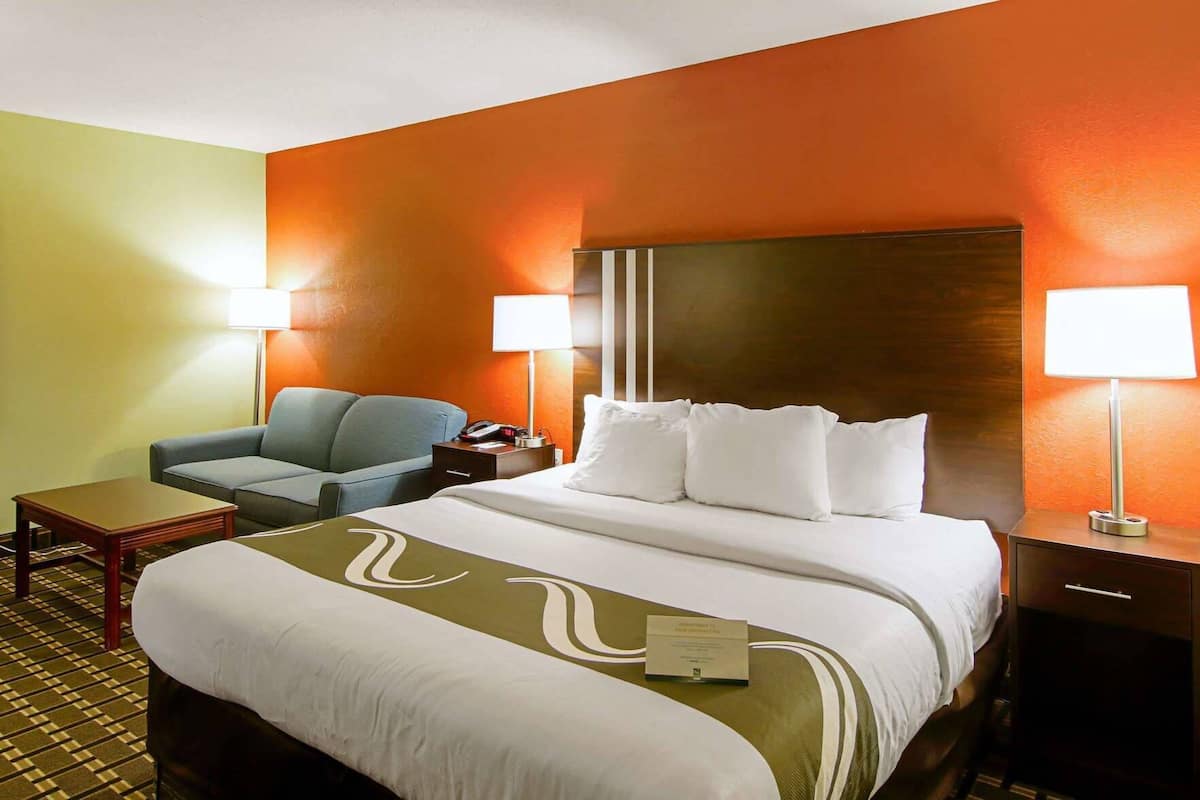A hotel room with a bed, a chair, a nightstand, and two lamps.
