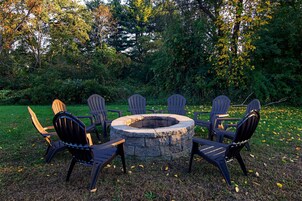 Un hogar circular de piedra rodeado por seis sillas Adirondack en un jardín.