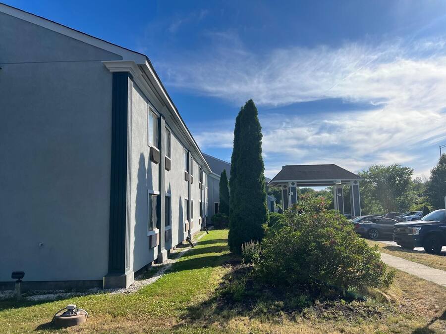 A residential building with a covered patio, a lawn, and parked cars.