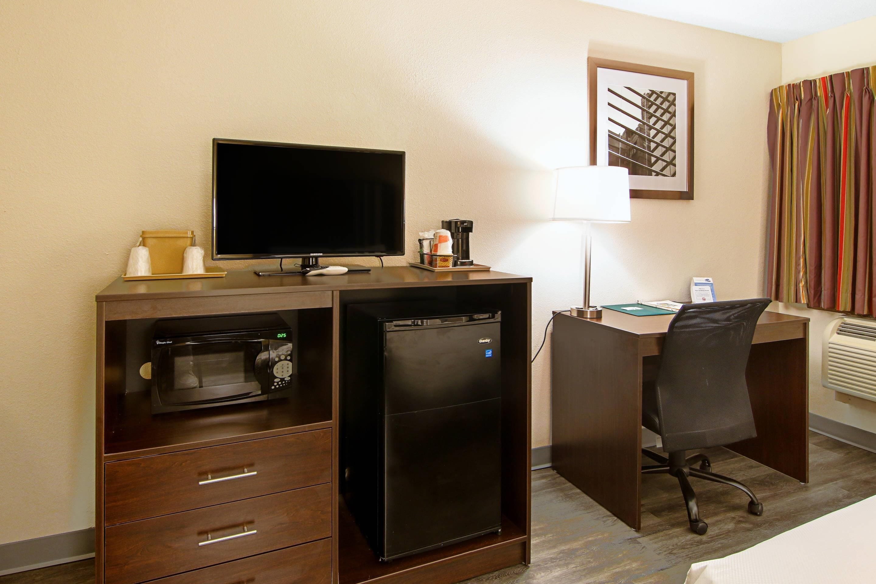 Hotelkamer met een bureau, televisie, magnetron, koelkast, stoel, lamp en bed.