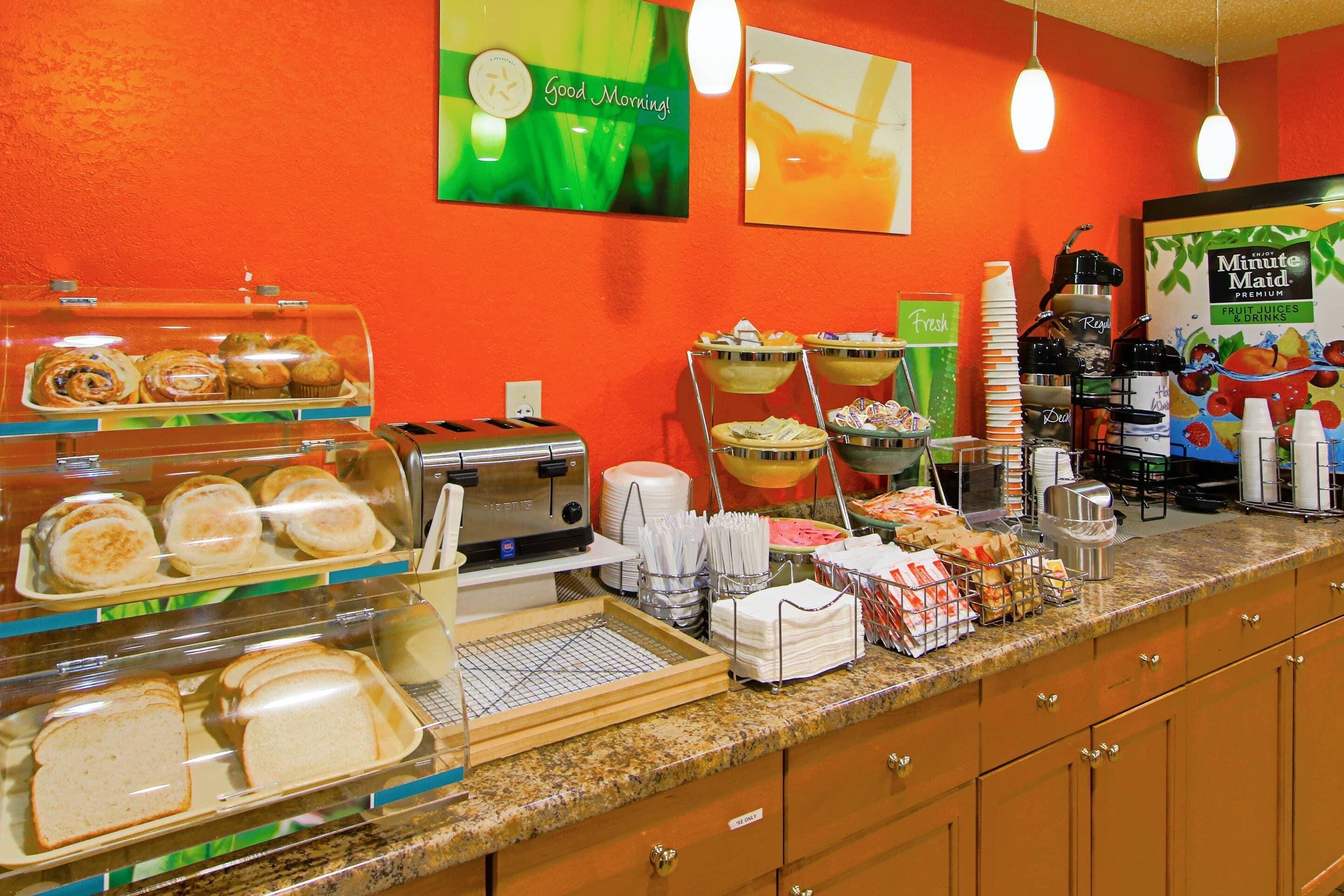 Un bufé de desayuno con diversas opciones de comida, una estación de café y un letrero que dice '¡Buenos días!'.