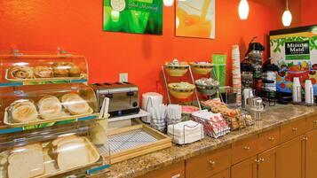Un bufé de desayuno con diversas opciones de comida, una estación de café y un letrero que dice '¡Buenos días!'.
