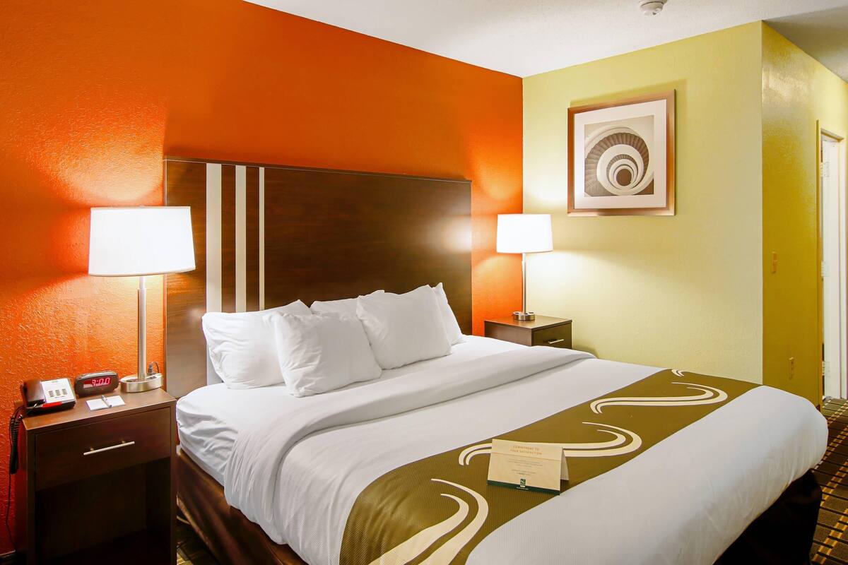 A hotel room with a bed, two bedside lamps, a clock, a nightstand, and a framed picture on the wall.