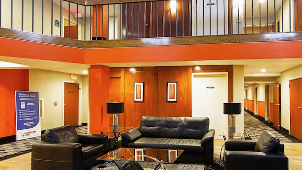 Un hall de hotel con una mesa de centro de vidrio, sofás de cuero, una escalera y un cartel.