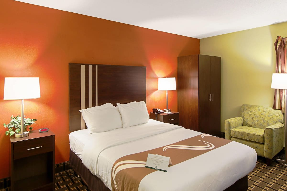 A hotel room with a bed, nightstands, a chair, and a wardrobe.