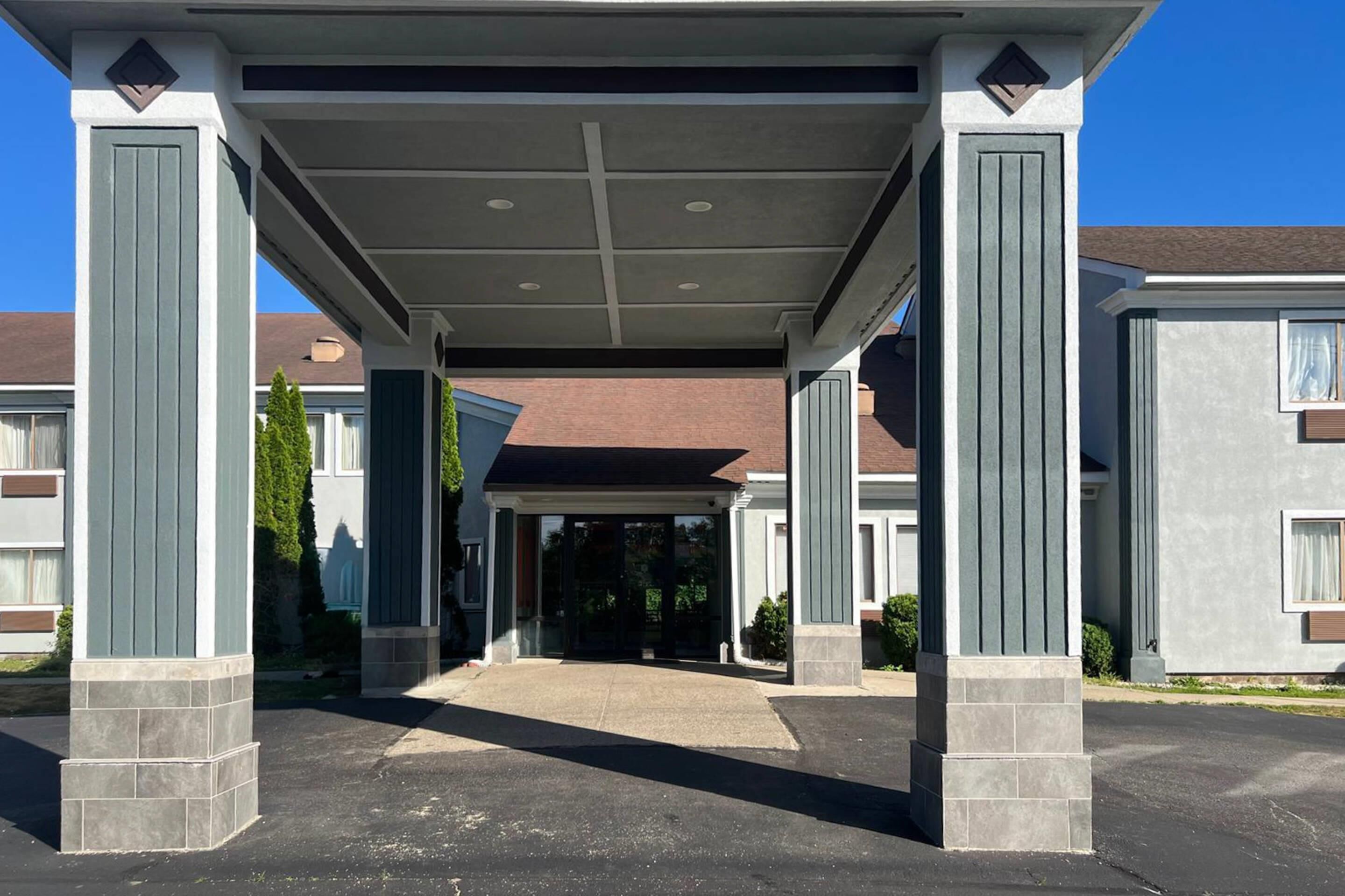 A covered entrance with columns, a driveway, and a building with a brown roof.