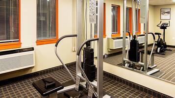 A gym with exercise equipment, a mirrored wall, and windows with blinds.