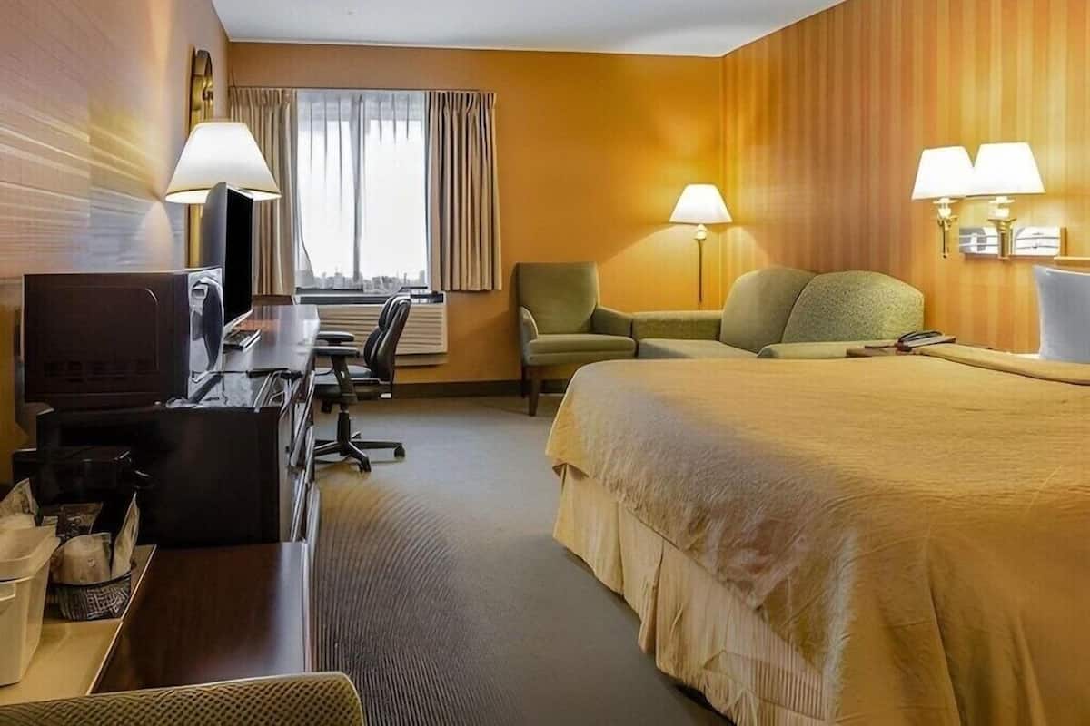 A hotel room with a bed, desk, chair, television, and lamps.