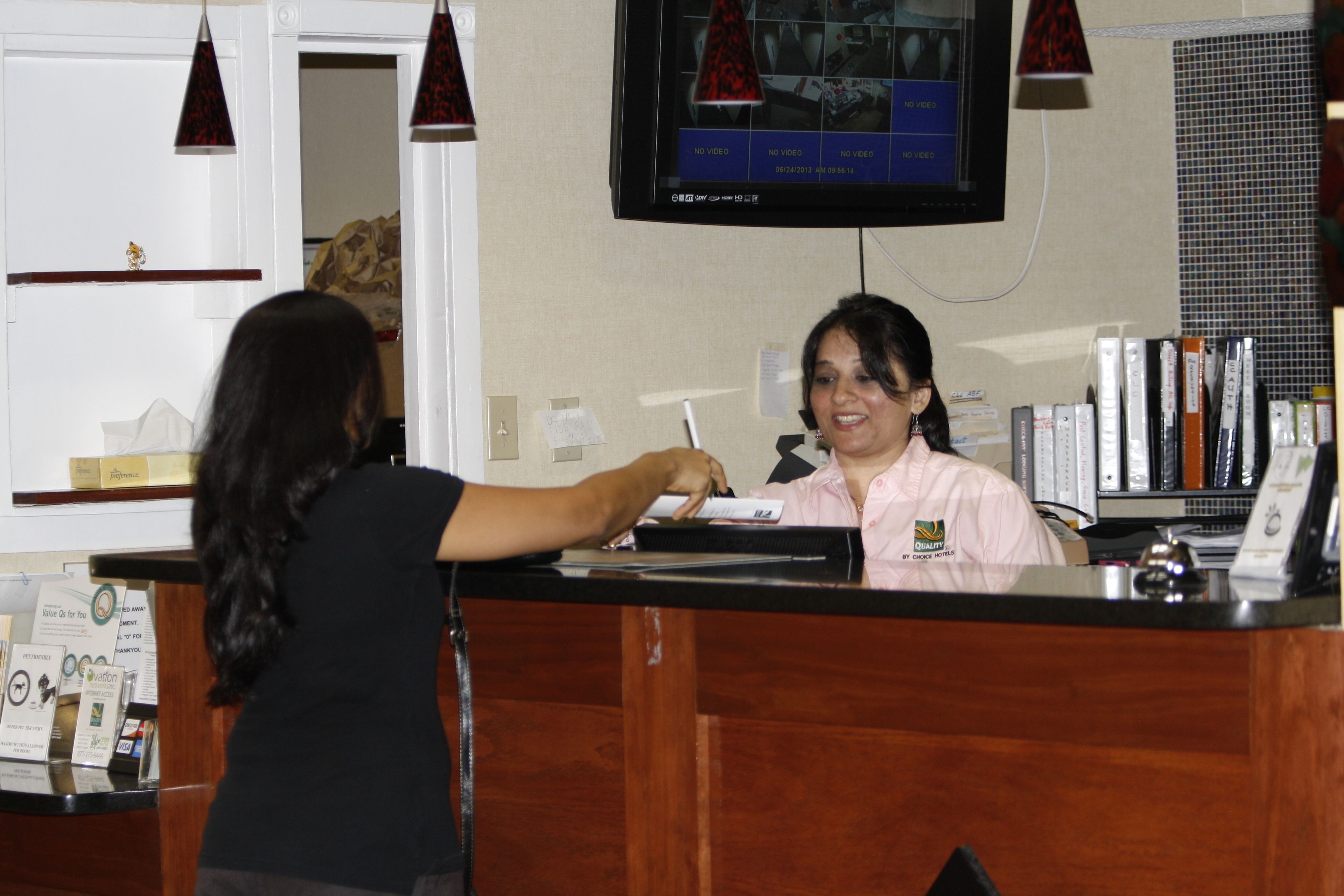 A reception desk with a monitor displaying a video feed, a counter, and a person interacting with the staff member.